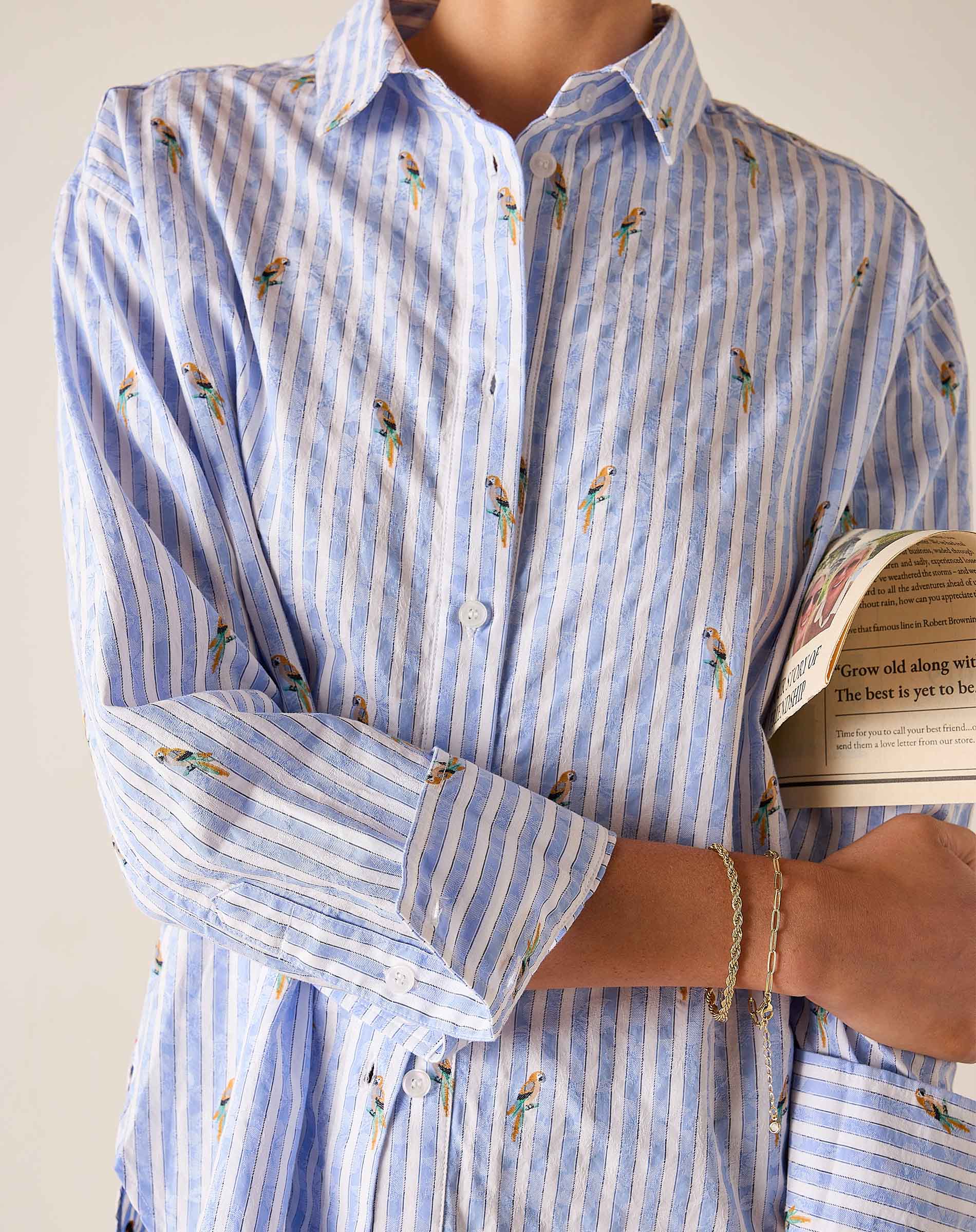 Person wearing a blue and white striped shirt with floral patterns, holding a book.