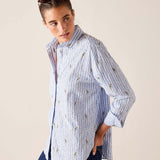 Woman wearing a blue and white striped shirt with floral patterns on a beige background