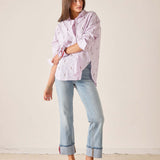 Woman wearing a pink striped shirt, light blue jeans, and red shoes against a beige background