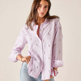 Woman wearing a pink striped shirt with floral patterns and light blue jeans against a beige background