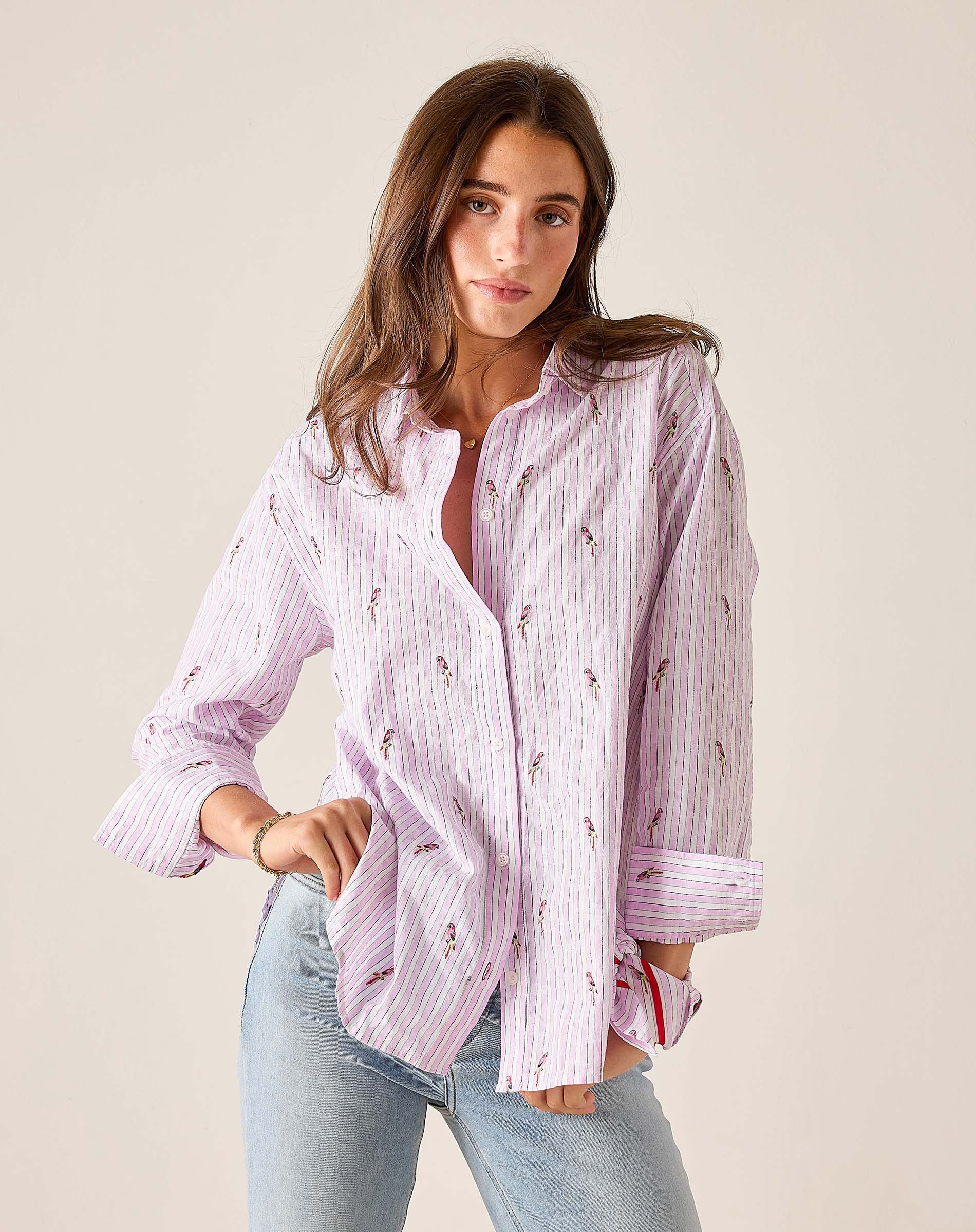 Woman wearing a pink striped shirt with floral patterns and light blue jeans against a beige background