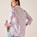Woman wearing a light purple patterned shirt with rolled-up sleeves against a plain background