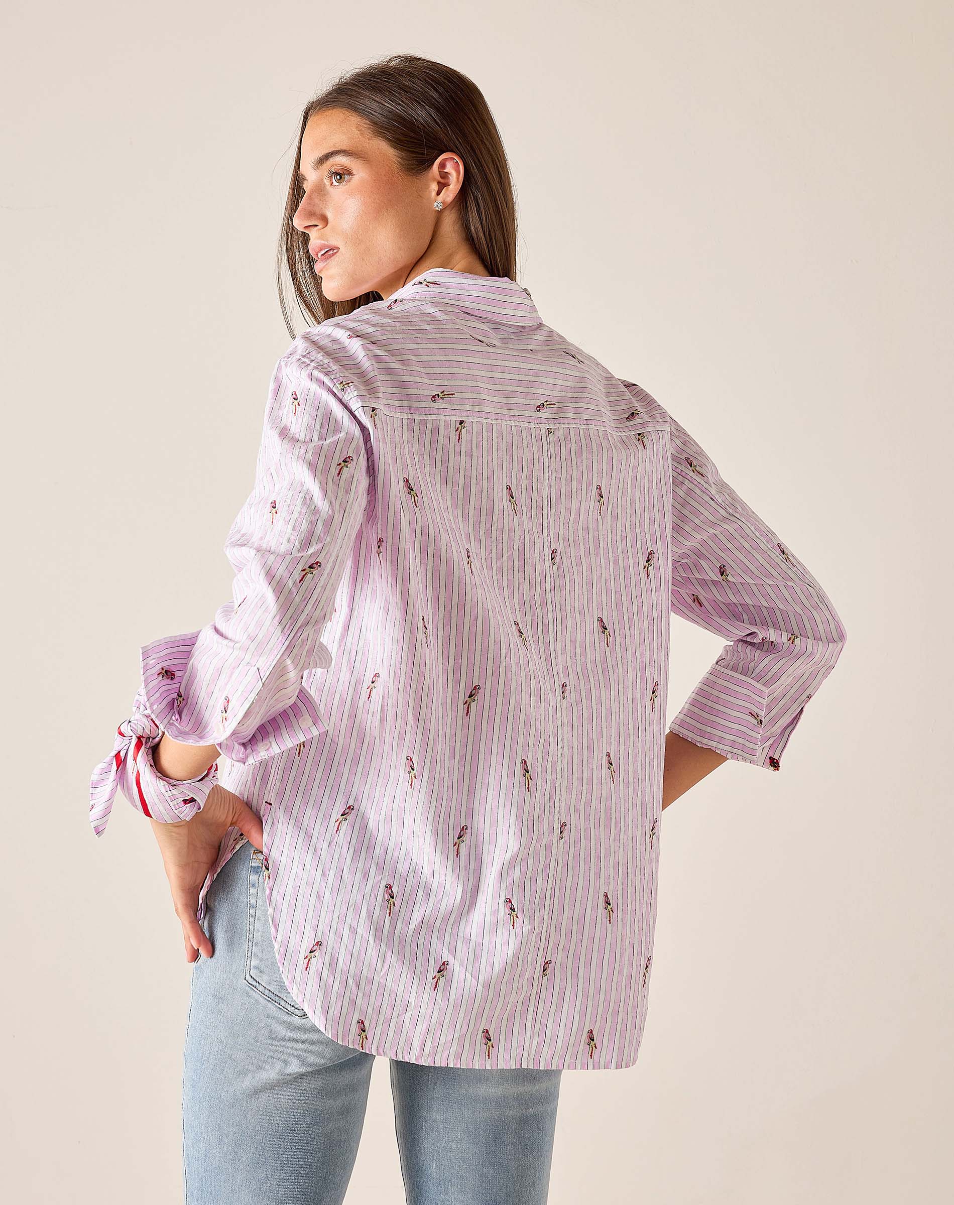 Woman wearing a light purple patterned shirt with rolled-up sleeves against a plain background