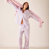 Woman wearing a pink and white patterned pajama set with a pink scarf against a plain background