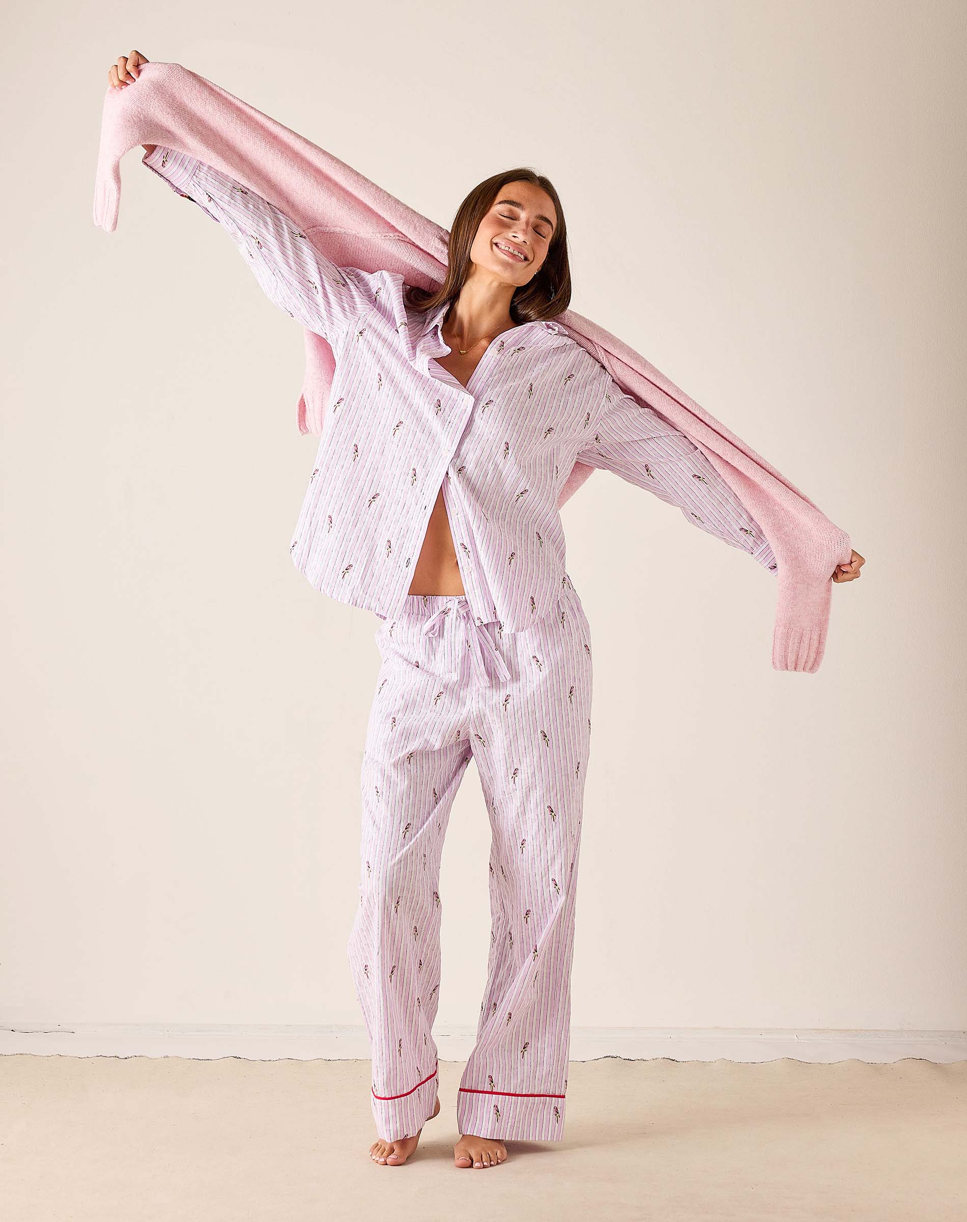 Woman wearing a pink and white patterned pajama set with a pink scarf against a plain background