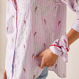 Close-up of a person wearing a pink and white striped shirt with small prints, holding their hand to their chest.