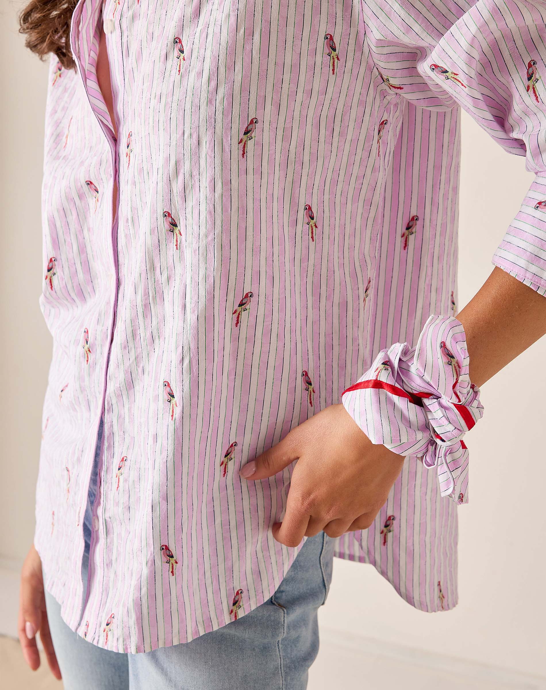 Close-up of a person wearing a pink and white striped shirt with small prints, holding their hand to their chest.