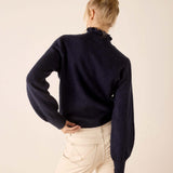 Back view of the navy blue knit sweater with a high neck and gathered sleeves.