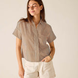 Woman wearing a striped shirt and white shorts against a beige background