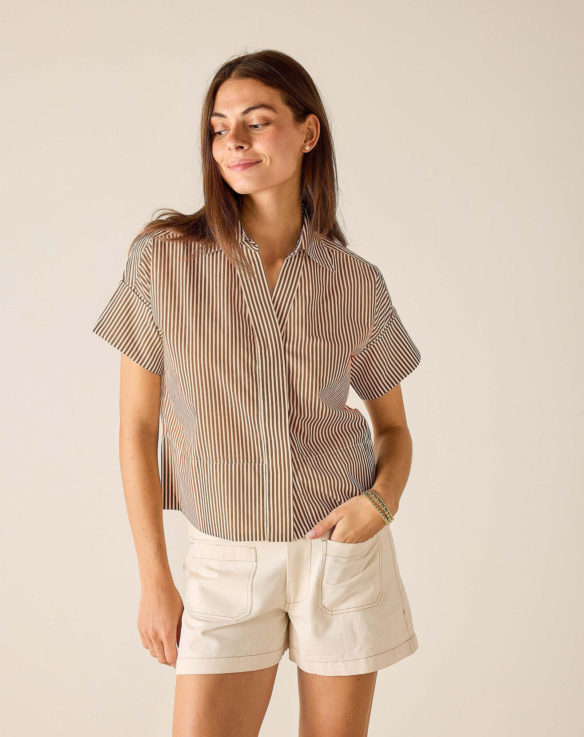 Woman wearing a striped shirt and white shorts against a beige background