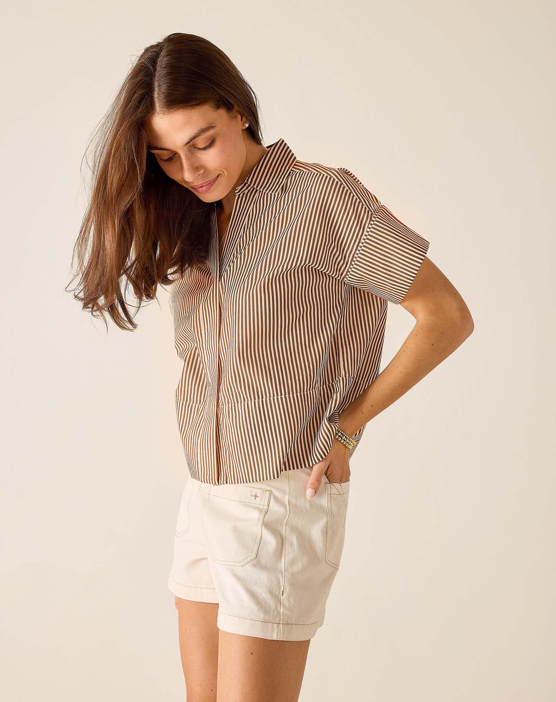 Woman wearing a striped shirt and white shorts on a plain background