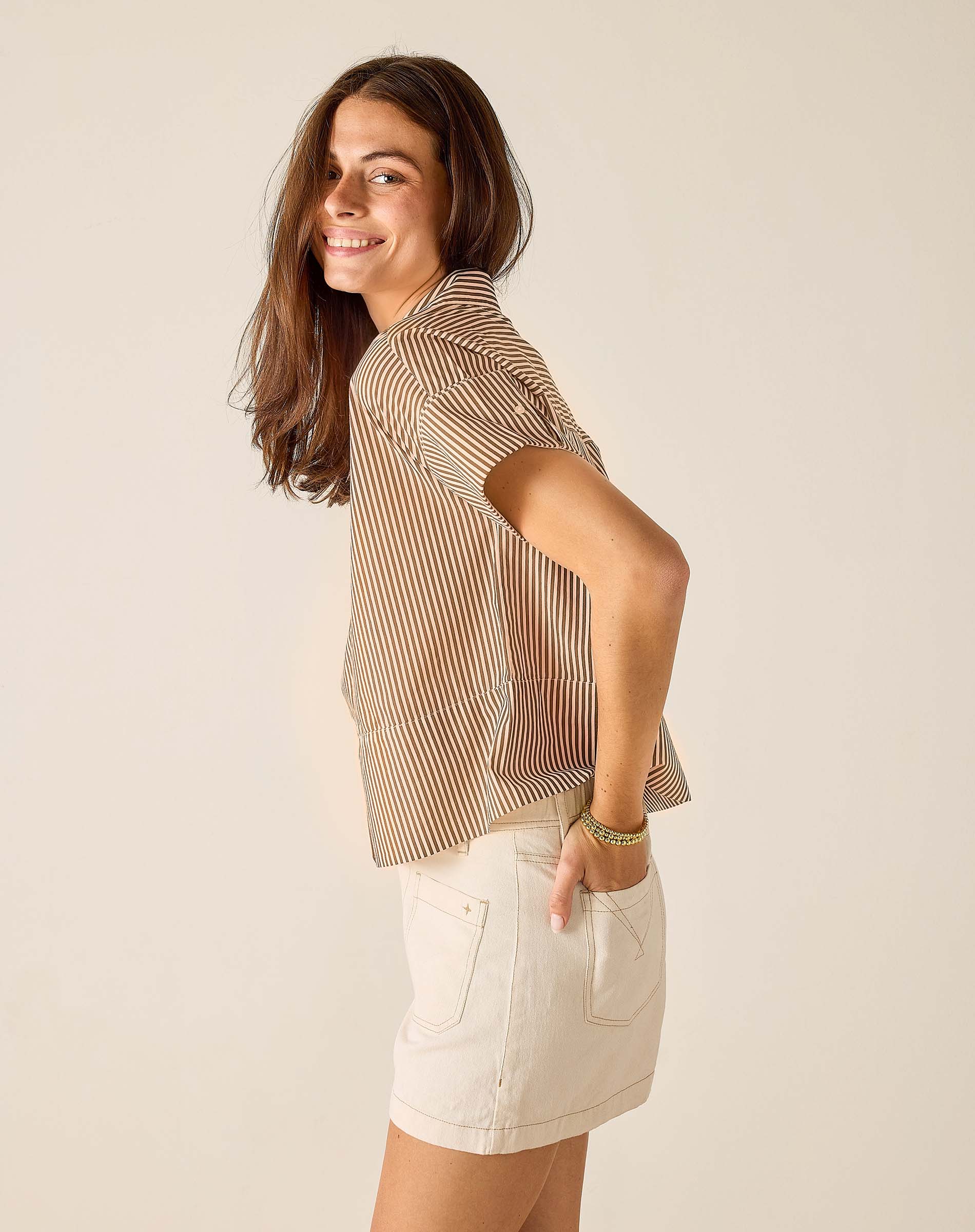 Woman wearing a striped shirt and white shorts against a plain background