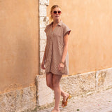 Woman in a brown dress standing against a beige wall on a sunny day.