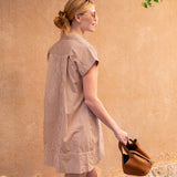 Woman in a striped dress holding a brown bag against a beige wall.