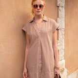 Woman wearing a striped dress and sunglasses against a stone wall.