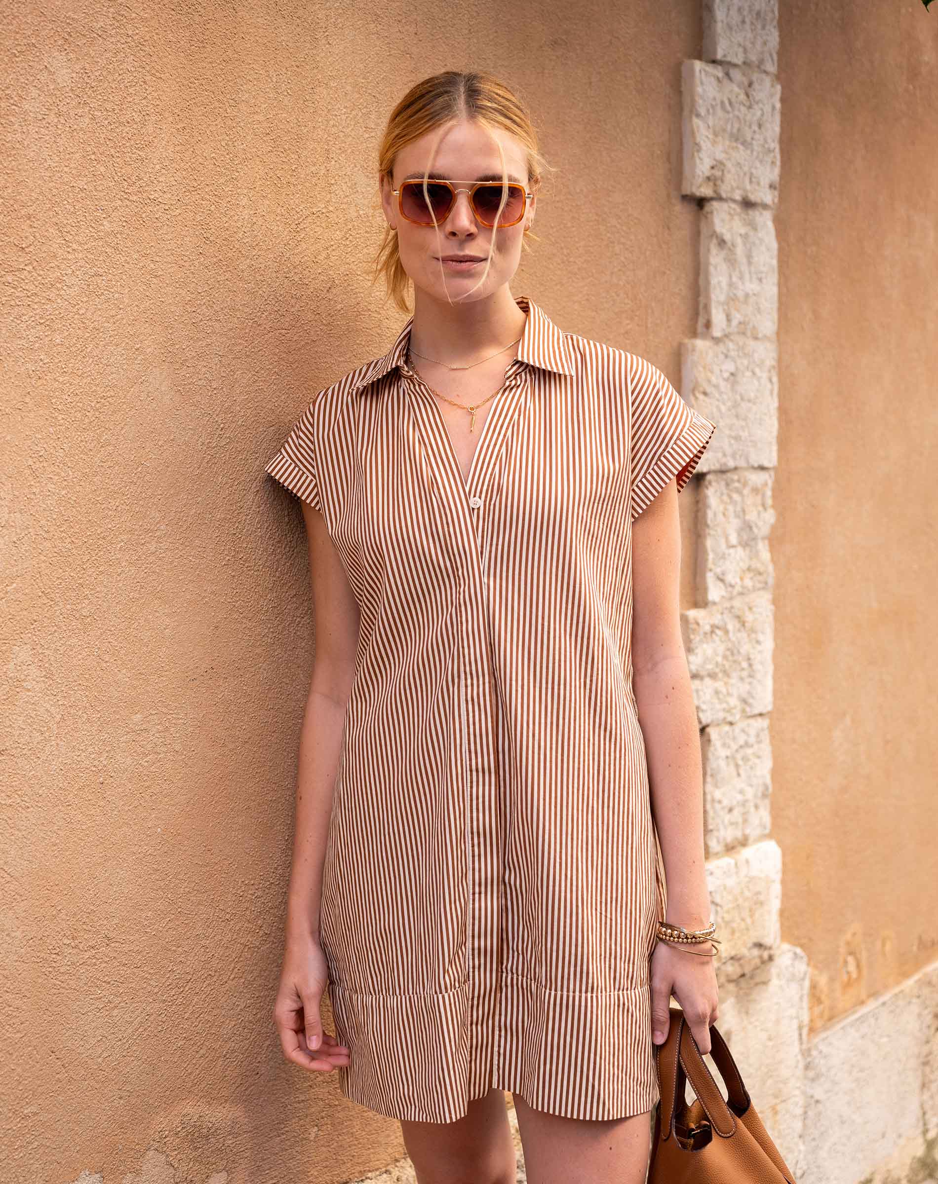Woman wearing a striped dress and sunglasses against a stone wall.