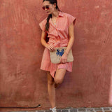 Woman in a pink dress holding a clutch with a blue crab design against a red wall.
