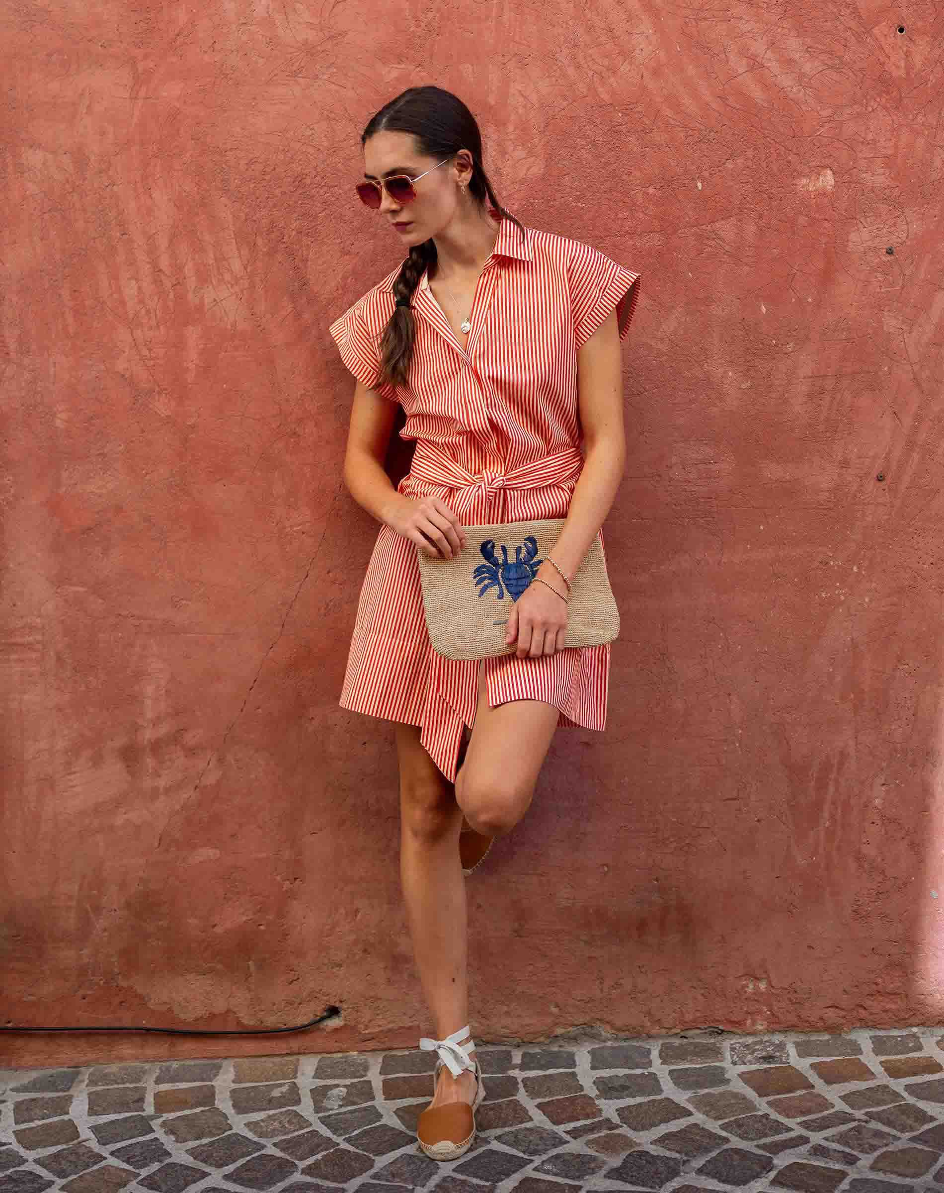 Woman in a pink dress holding a clutch with a blue crab design against a red wall.