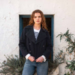 female wearing navy peacoat over white and blue striped tee shirt with blue jeans on white wall