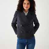 female wearing navy twill peacoat over a white collared shirt with blue jeans on a white background