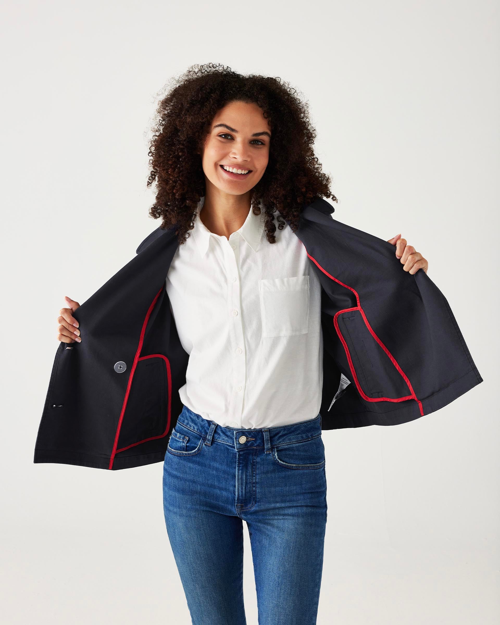 female wearing navy twill peacoat over a white collared shirt with blue jeans on a white background