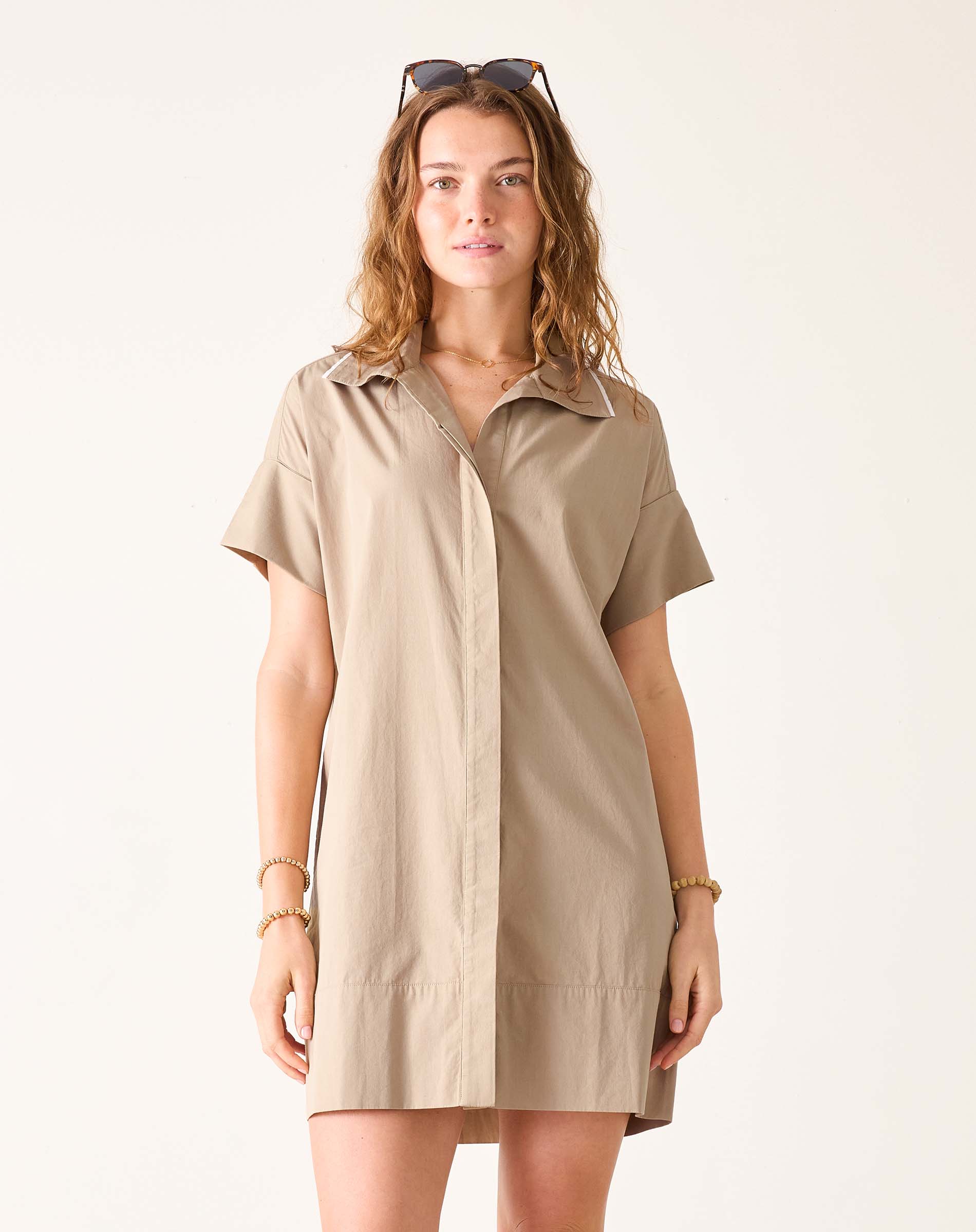 Model wearing a khaki-colored short-sleeved shirt dress with wide hems and a buttoned front.