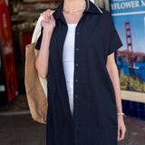 A model wears a navy blue short-sleeve sailor dress with a white collar and a large tote bag.