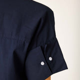 Detail of a navy blue sailor-style dress with a wide hem and buttoned sleeve detail.