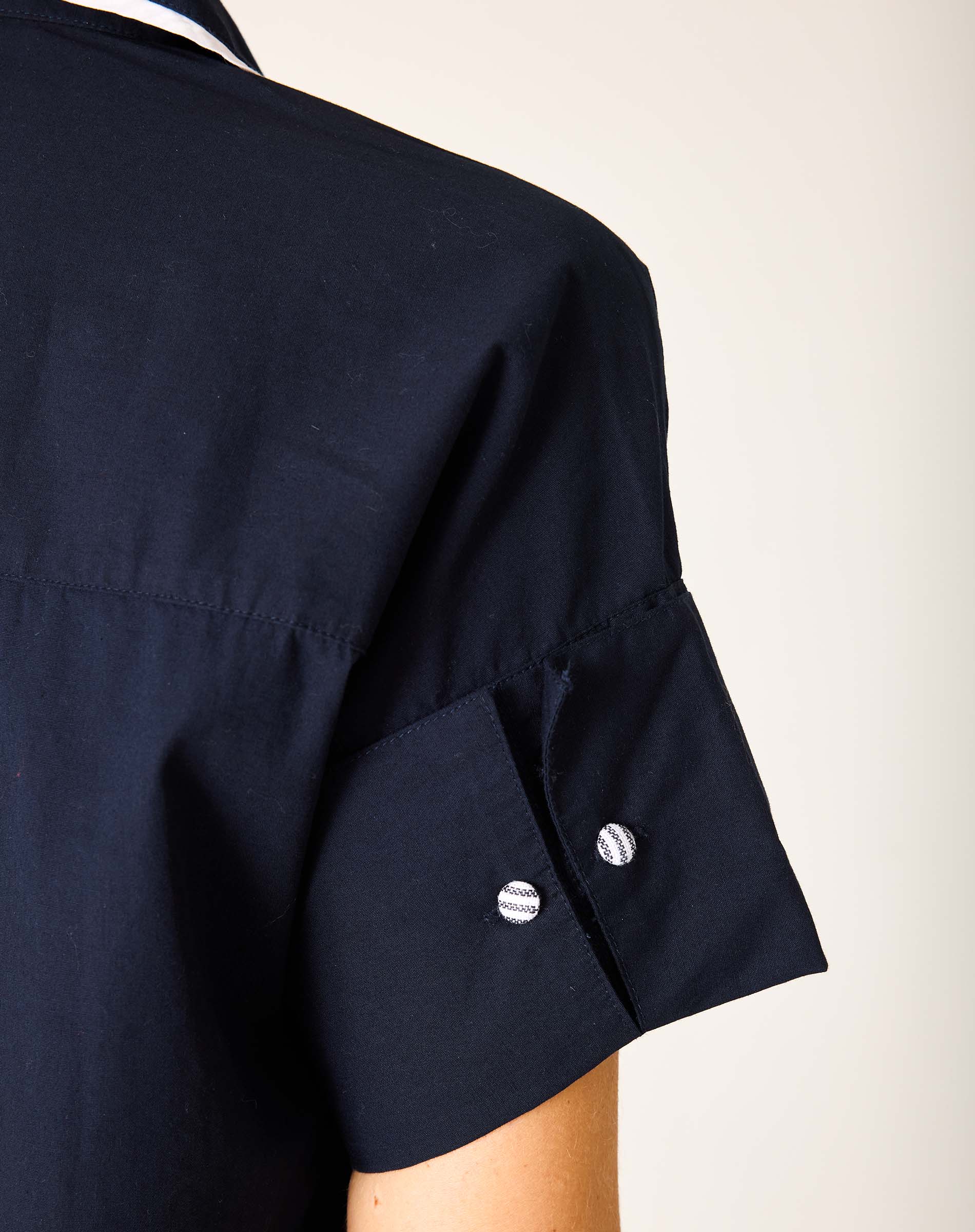 Detail of a navy blue sailor-style dress with a wide hem and buttoned sleeve detail.
