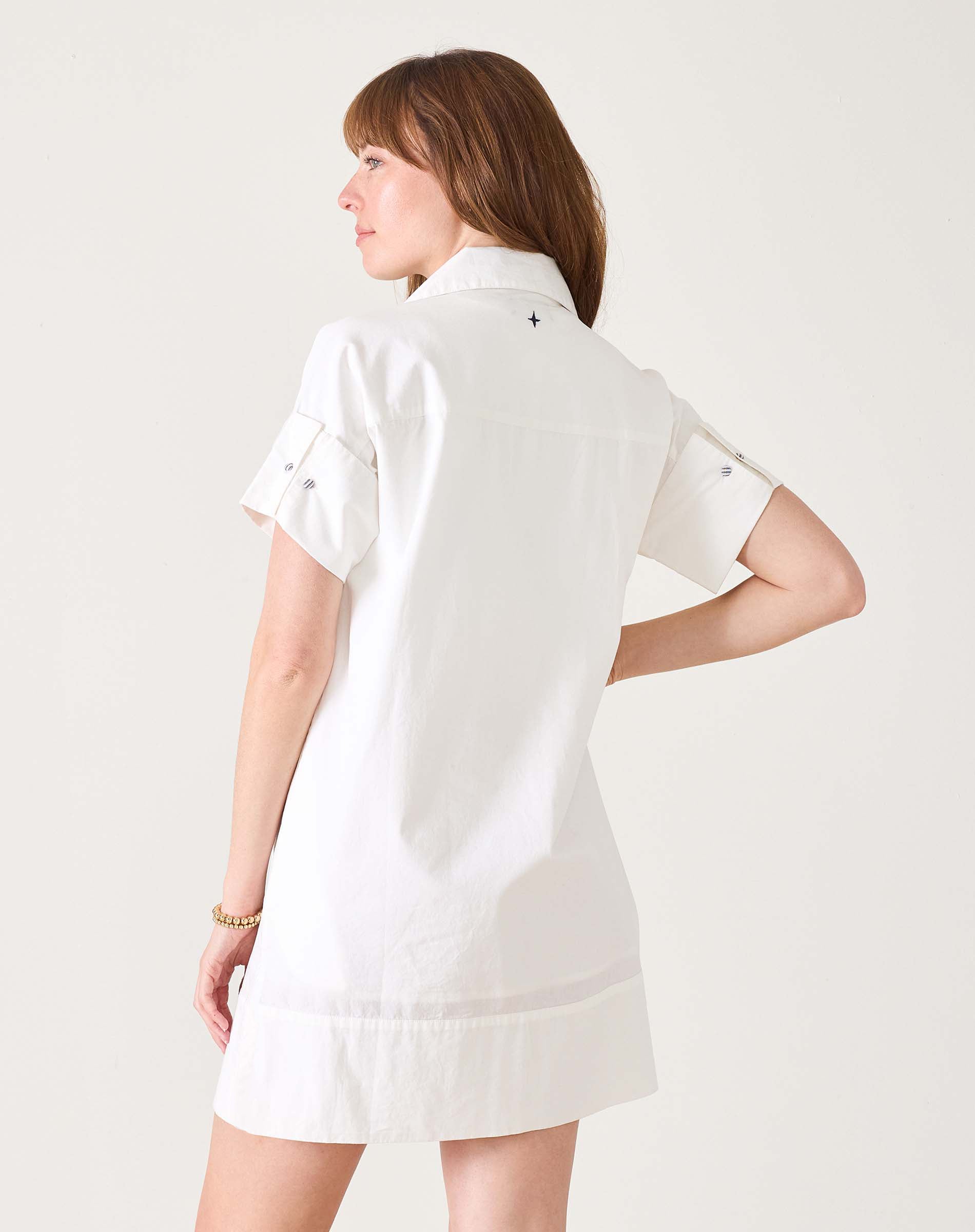 Woman in white short-sleeved sailor dress with a wide hem and button details on the sleeves.