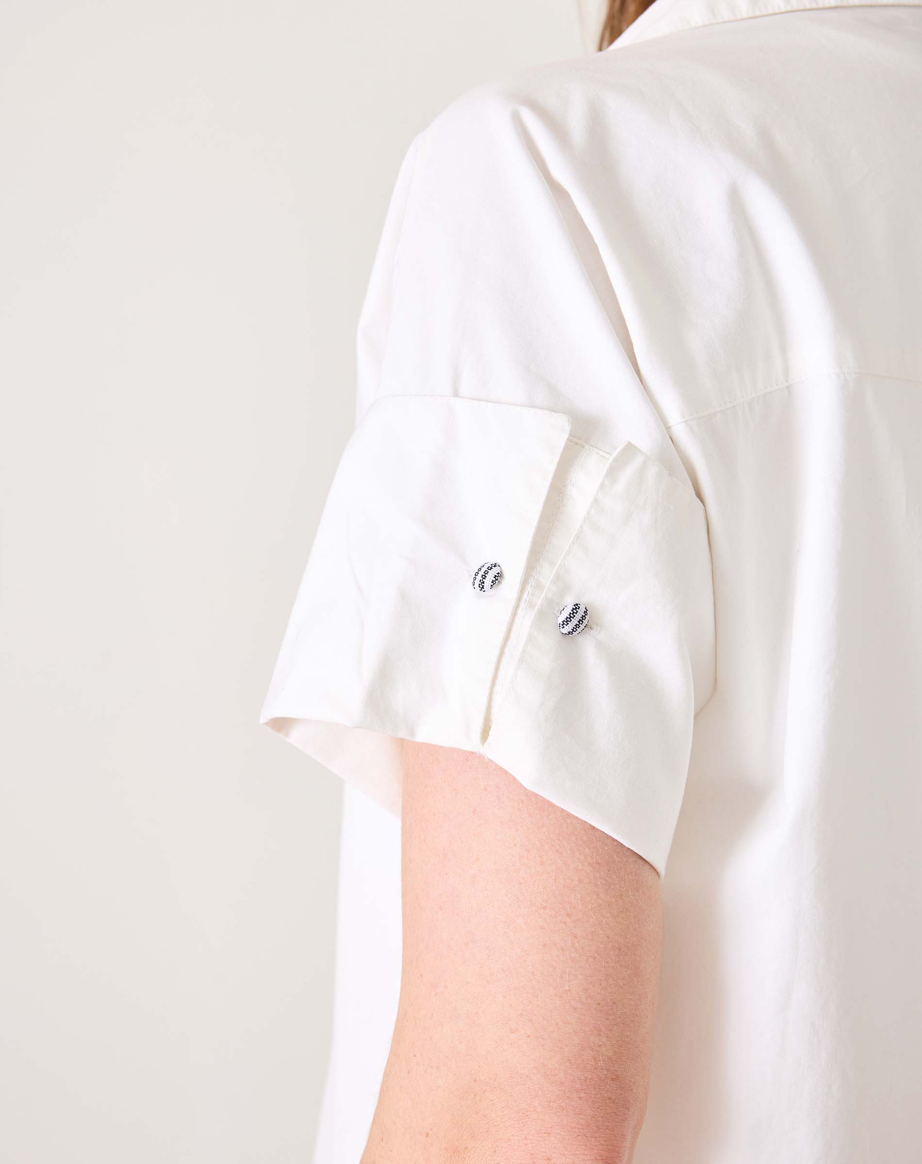 Detail of the white sailor-style wide hem dress featuring a rolled sleeve with button details.
