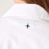 Woman in a white dress featuring a small navy blue embroidered sail detail on the shoulder.