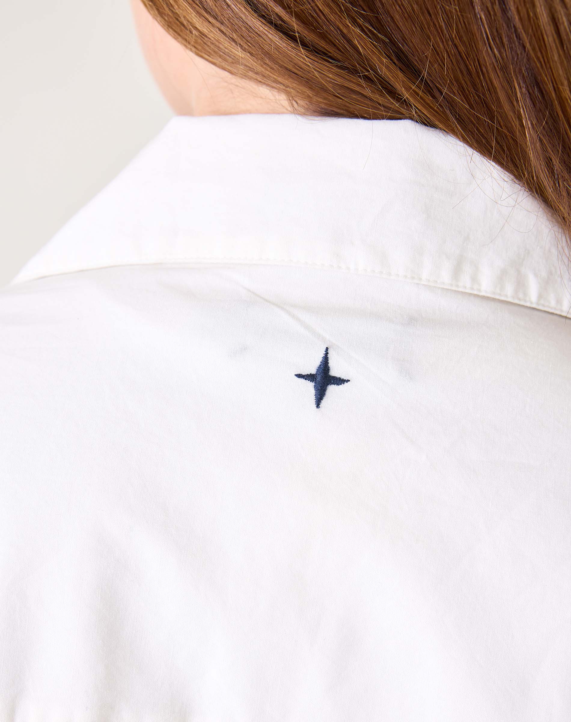 Woman in a white dress featuring a small navy blue embroidered sail detail on the shoulder.