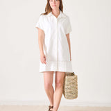Model wearing a white short-sleeve sailor dress with a wide hem and a woven beach bag.