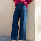 Person wearing a red sweater and blue jeans standing against a beige wall.