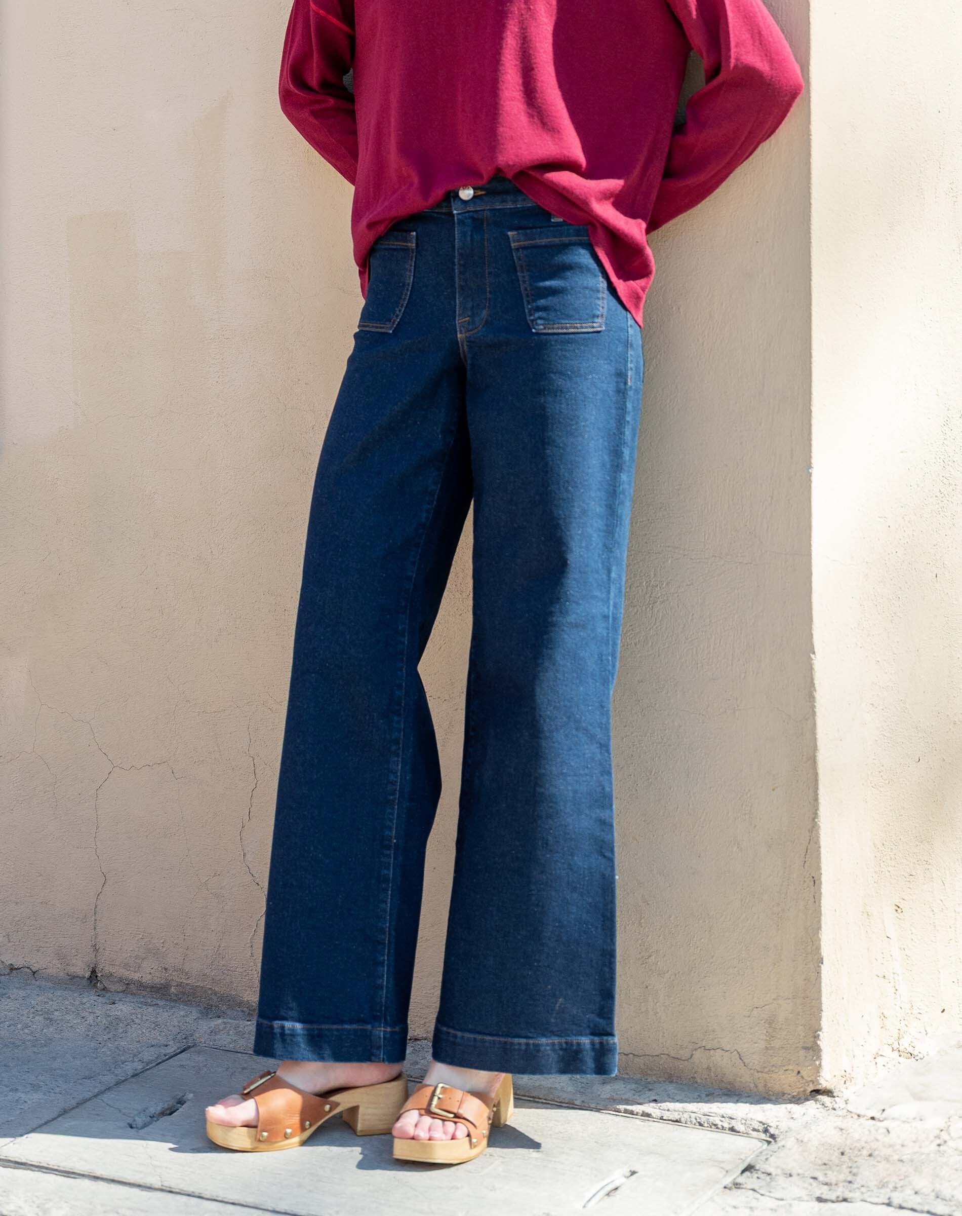 Person wearing a red sweater and blue jeans standing against a beige wall.