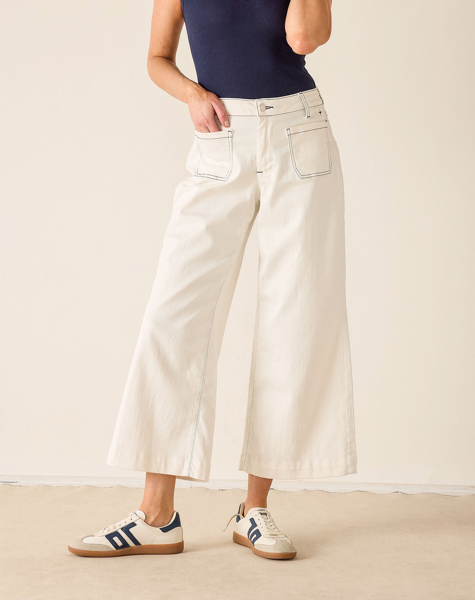 Person wearing white wide-leg jeans and Adidas shoes on a plain background