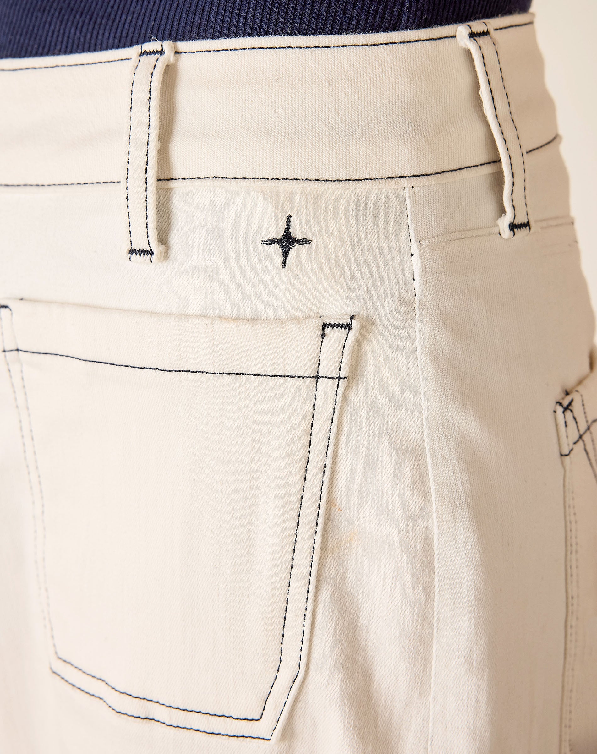 Close-up of beige pants with a brand logo on the pocket.