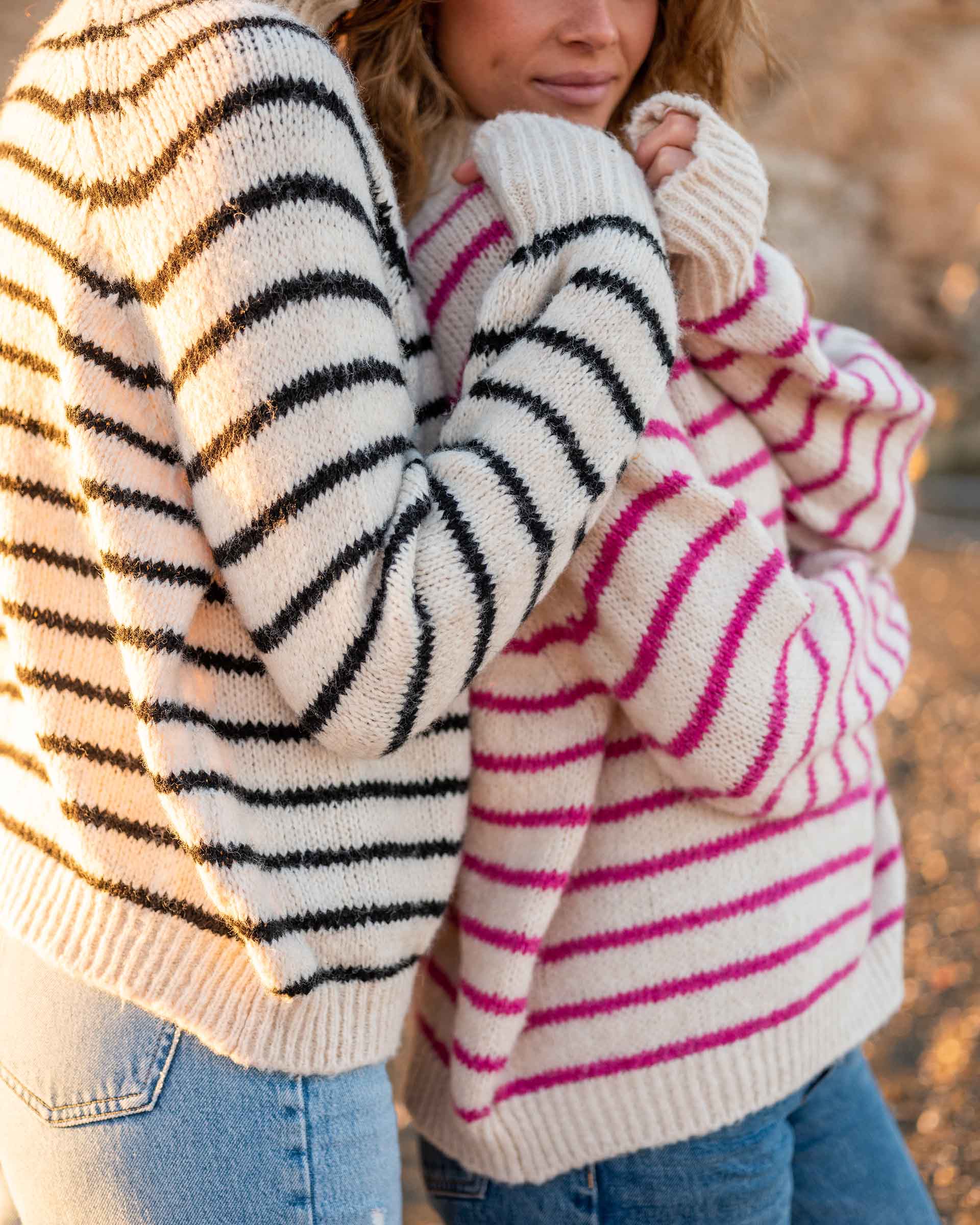 two women wearing mersea salt and sea turtlenecks in buttercream and stripes standing together in front of rocks