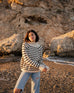 woman wearing mersea salt and sea turtleneck in buttercream and black stripe standing on beach in front of cliff