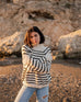 woman wearing mersea salt and sea turtleneck in buttercream and black stripe standing with arms crossed on beach in front of cliff