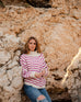 woman wearing mersea salt and sea turtleneck in buttercream and magenta stripe leaning against rocks