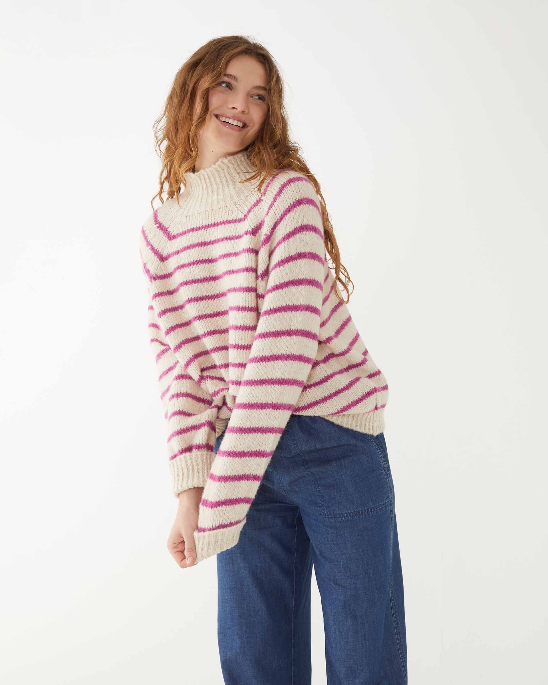 smiling woman wearing mersea salt and sea turtleneck in buttercream and magenta stripe standing leaning against white background