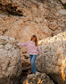 woman wearing mersea salt and sea turtleneck in buttercream and magenta stripe walking on rocks 