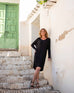 female wearing long sleeve v neck sweater dress with black sandals on stairs leaning on a wall