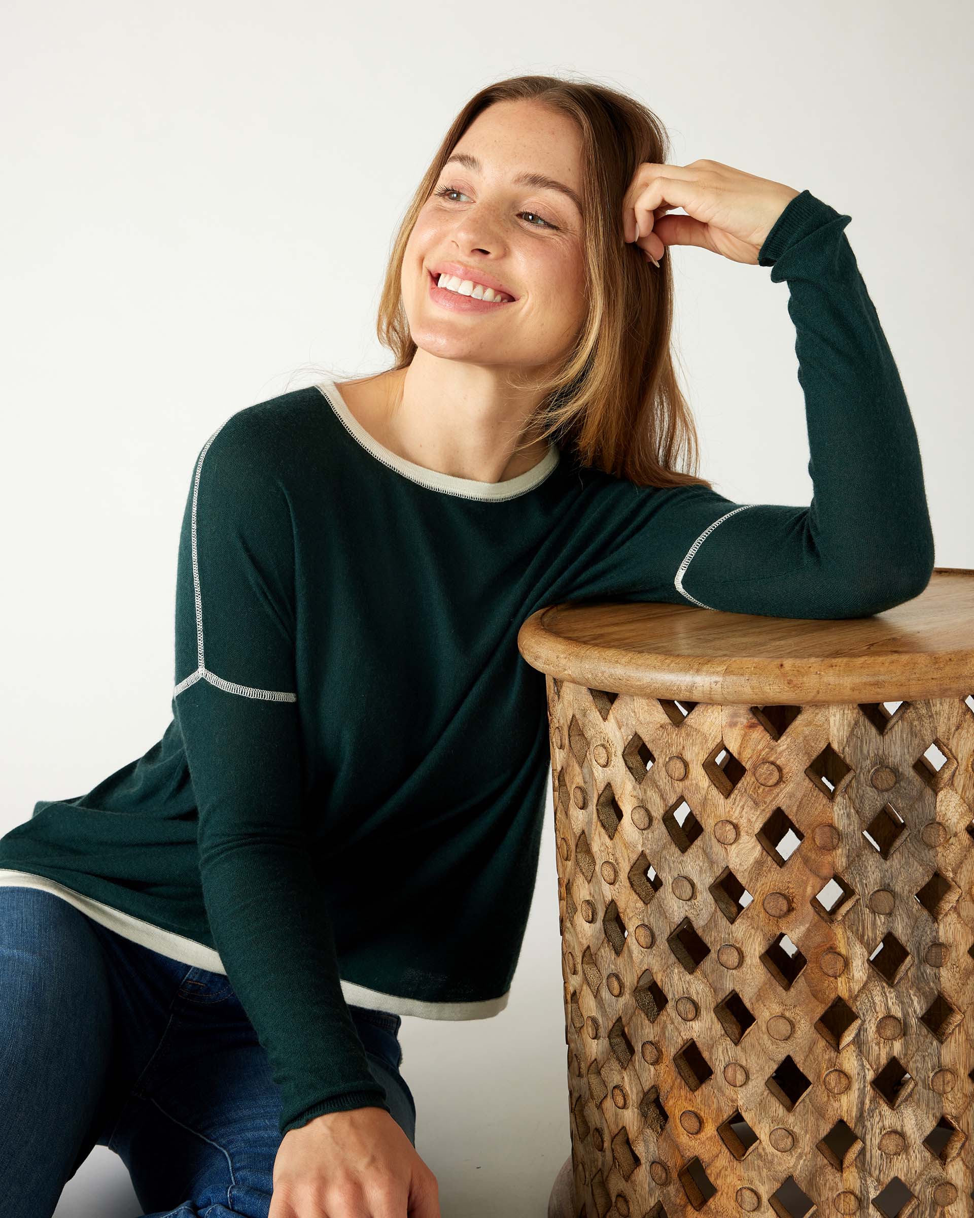 woman wearing mersea saltwash sweater in forest green leaning against stool