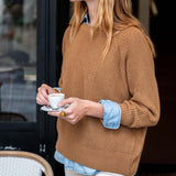 Woman in a brown sweater holding a cup of coffee outdoors.