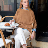 Woman sitting at an outdoor cafe table with a croissant and coffee.