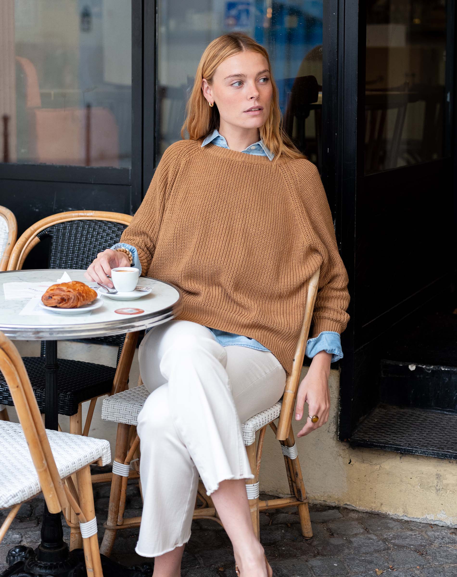 Woman sitting at an outdoor cafe table with a croissant and coffee.