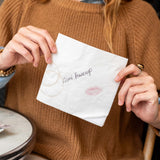 Person holding a white card with text and a lipstick mark, sitting at a table.